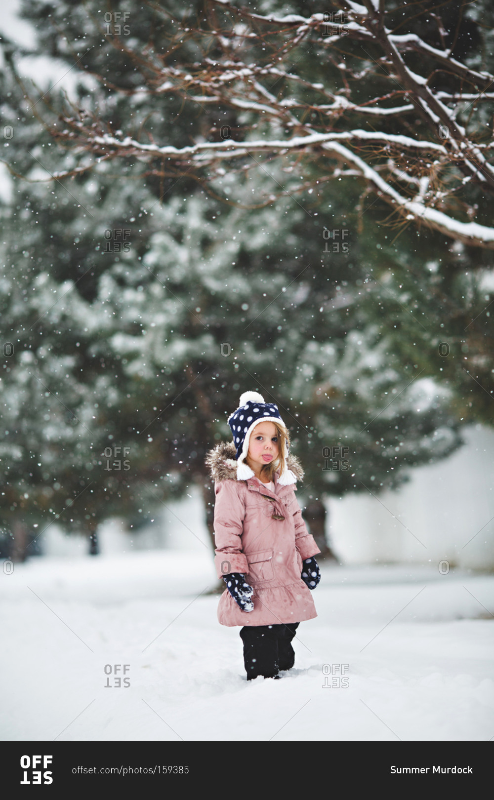 Young girl sticking out her tongue in the snowfall stock photo - OFFSET