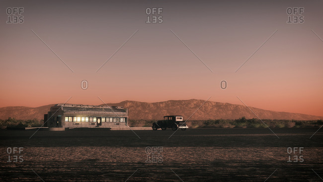 Desert landscape with desolate diner and vintage car at sunset