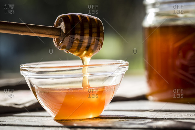 Honey dripping off a honey spoon into a glass bowl