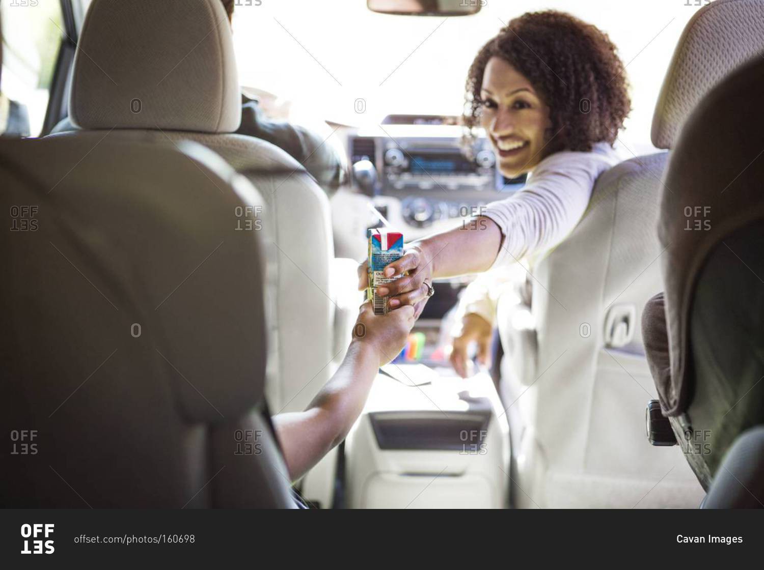 A mom hands her son a juice box in a van