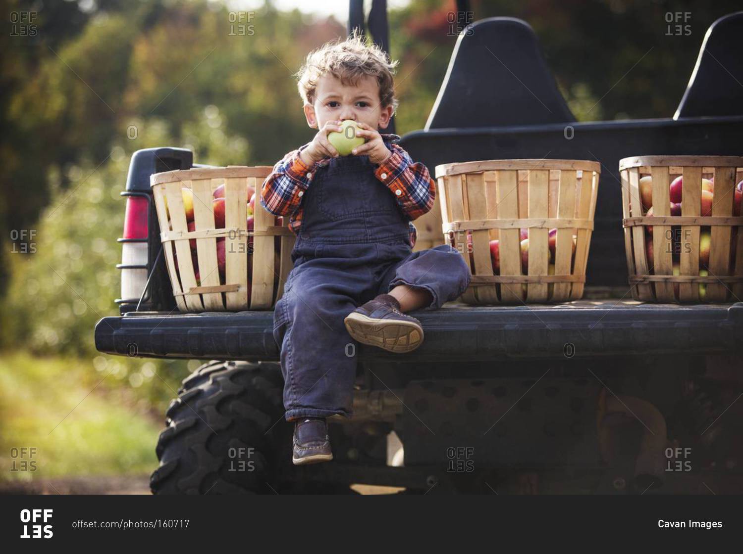 A boy eats an apple in the back of a pickup truck