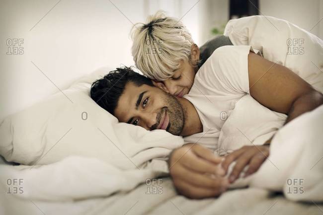 A woman cuddles her boyfriend in bed