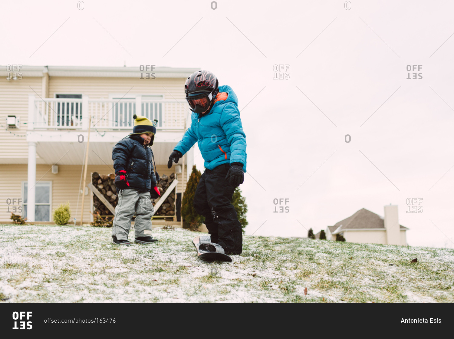 Two boys snowboarding in the backyard