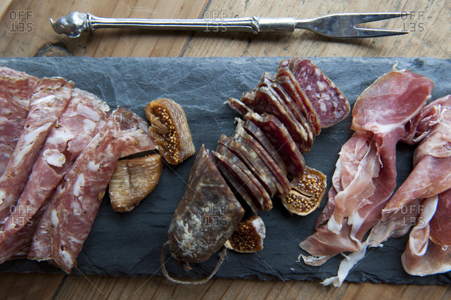 Overhead view of cured meats and figs on slate board