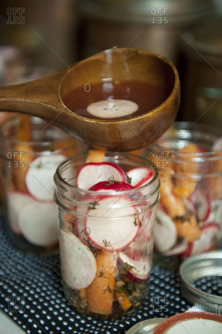 Pouring vinegar into jar to pickle carrots and radishes