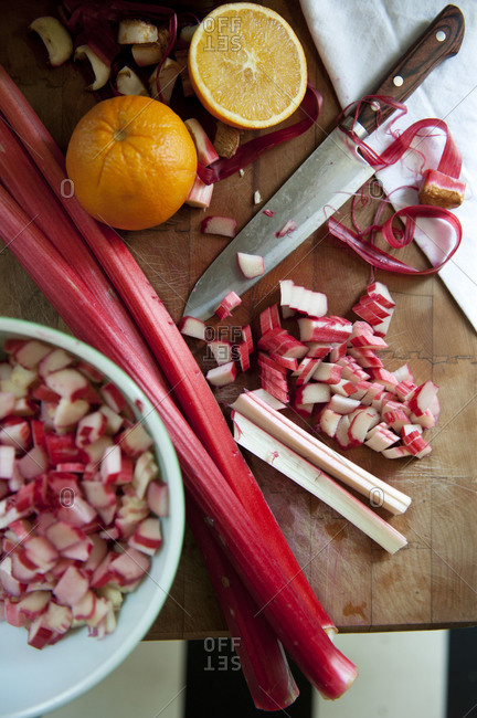Overhead view of rhubarb and oranges being cut on butcher block