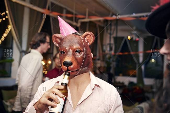 Man Wearing Bear Mask And Party Hat Drinks A Beer At A Party Stock