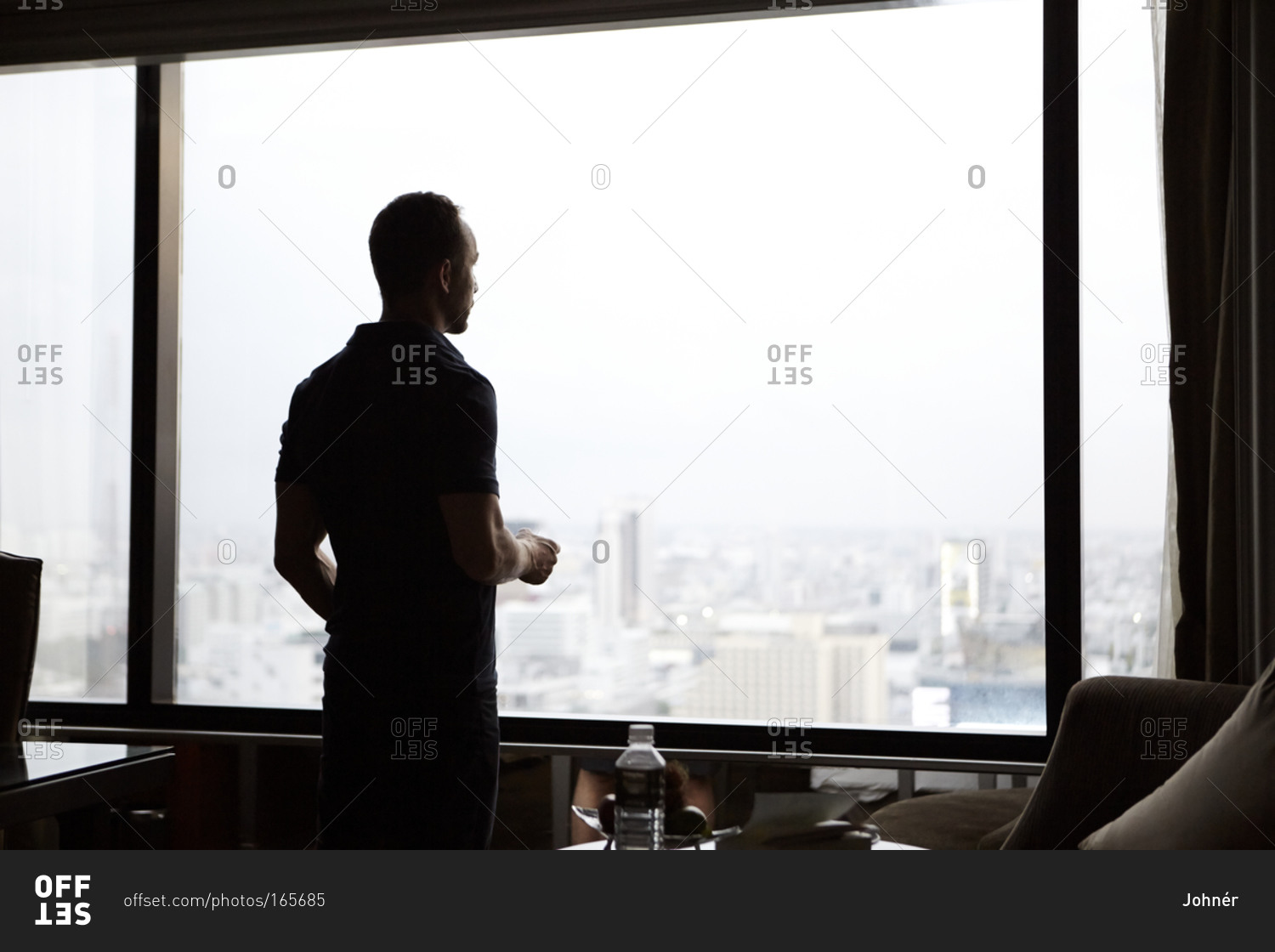 Man looking through window at cityscape stock photo - OFFSET