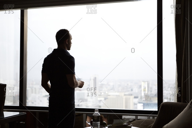 Man looking through window at cityscape stock photo - OFFSET