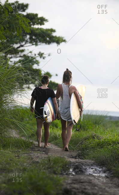 Two women with surfboards walking along footpath, Bali
