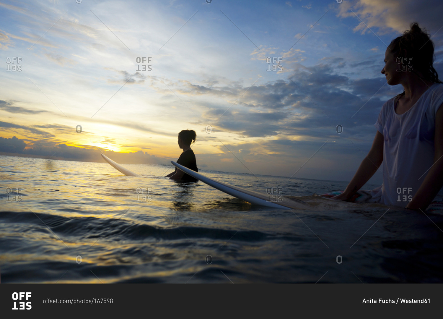 Two female surfer in the water watching sun, Bali