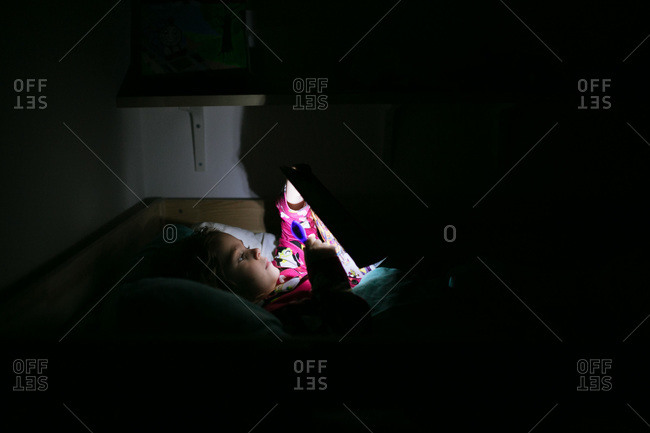A girl reads a book by flashlight