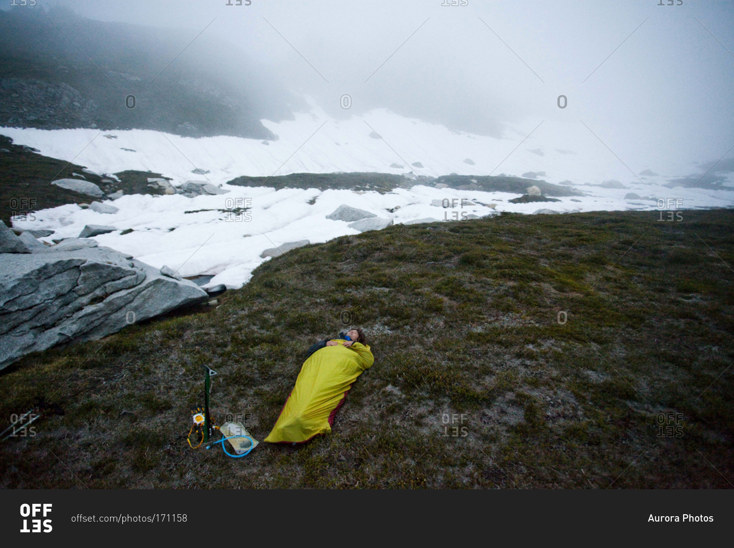 A climber sleeps outside in a bivy sack underneath a cloudy sky