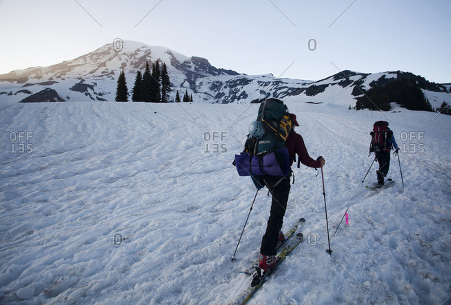 Two skiers skin up a snowy trail as the sun sets over the distant  mountains