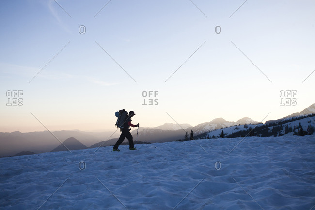 One skier skins up a snowy trail as the sun sets over the distant  mountains