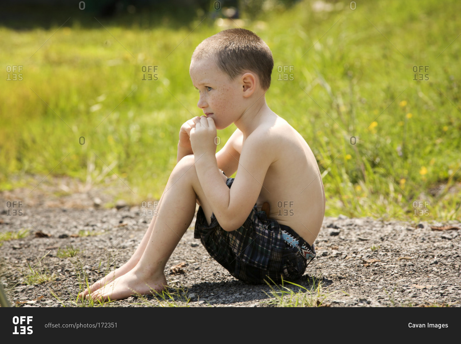 Boy sitting on the ground outdoors stock photo - OFFSET