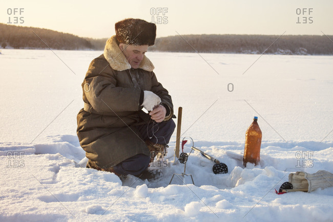 Man sitting next to ice fishing hole - Stock Image - Everypixel