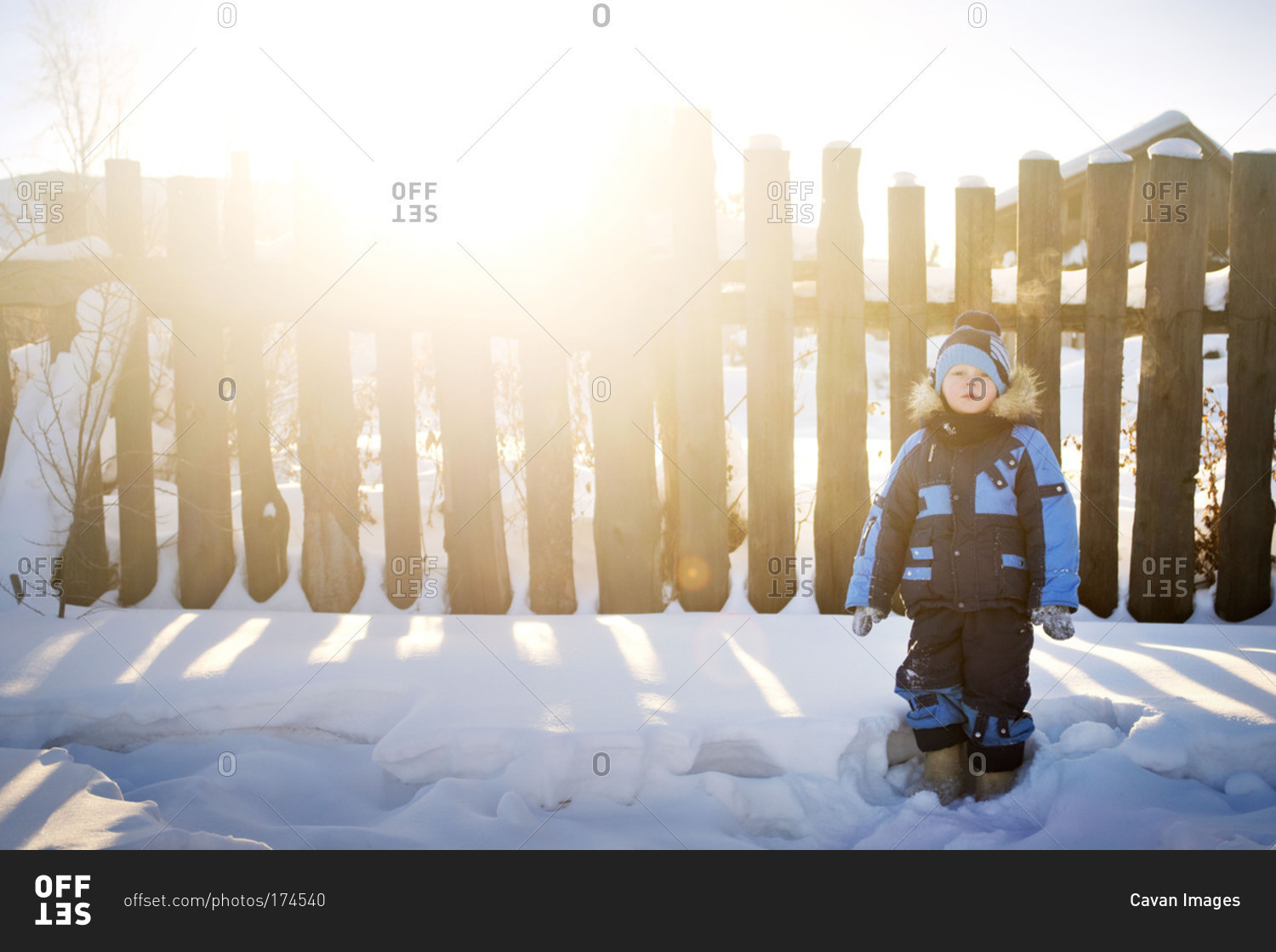 Young boy standing in snow by fence