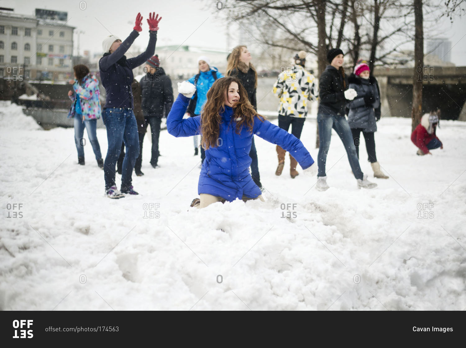 Young woman throwing snowball in snowball fight stock photo - OFFSET