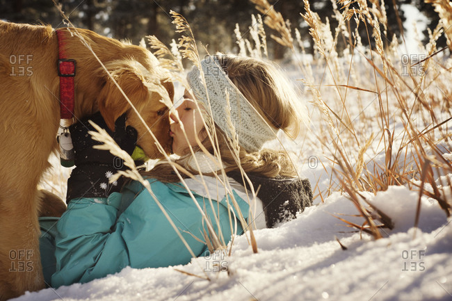 Young woman kissing retriever on snout in snow