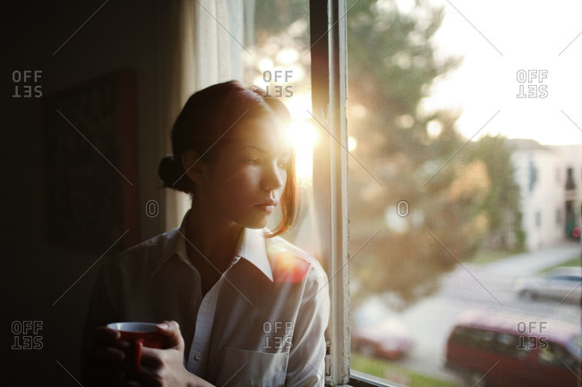 Young woman having cup of tea by window
