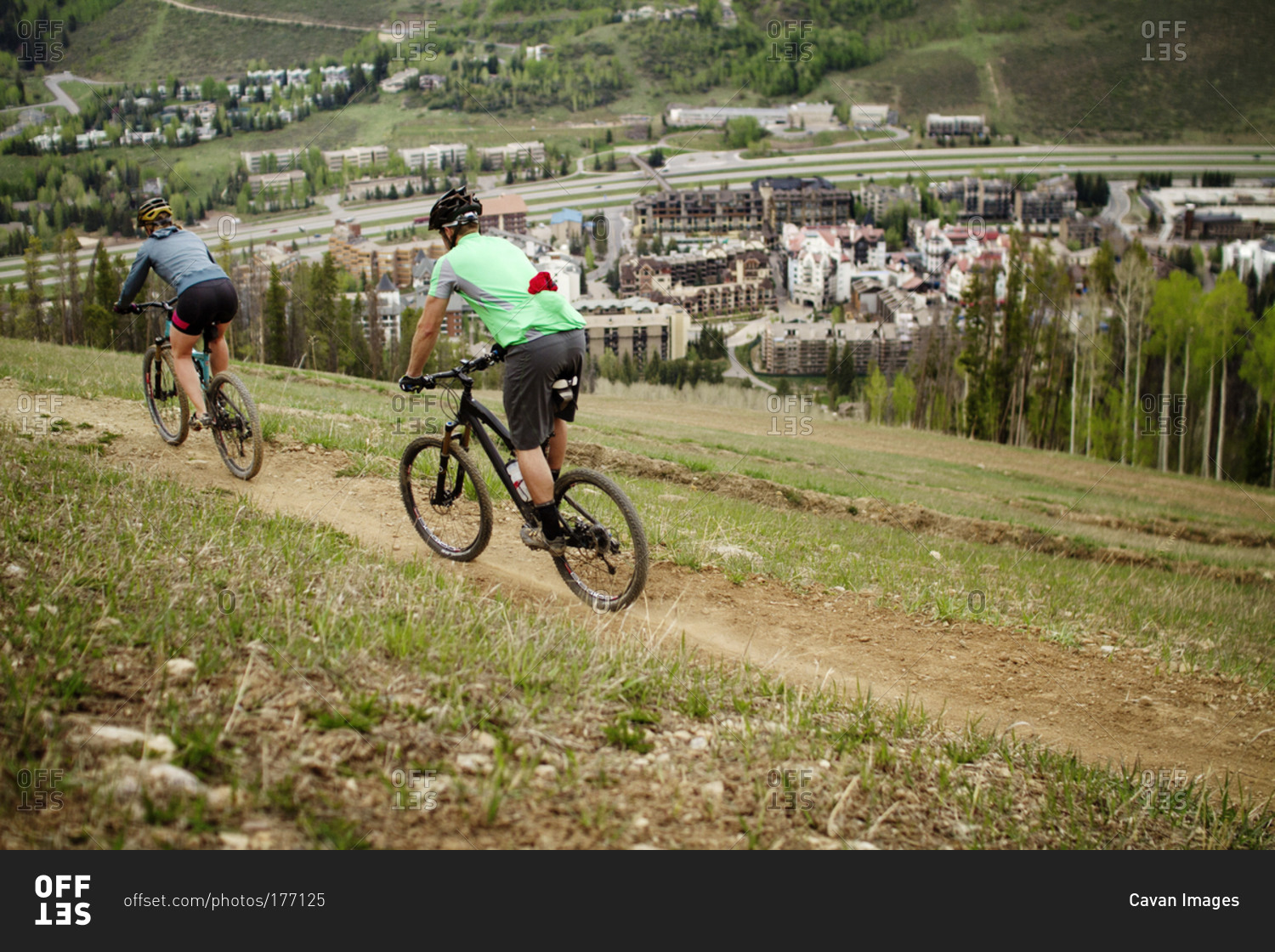 A couple mountain biking past a town