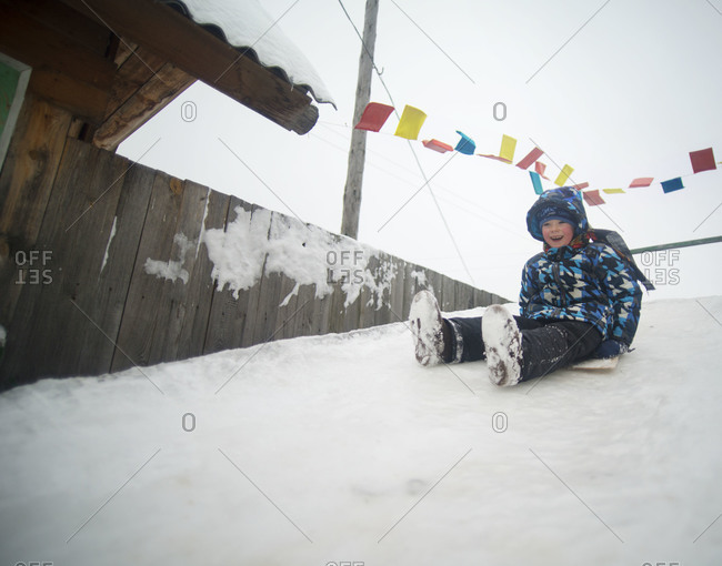 Happy toddler boy sliding down snow in the mountains stock photo - OFFSET