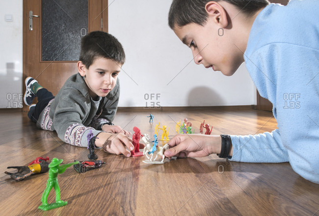 Two boys playing with miniature figurines on the floor at home