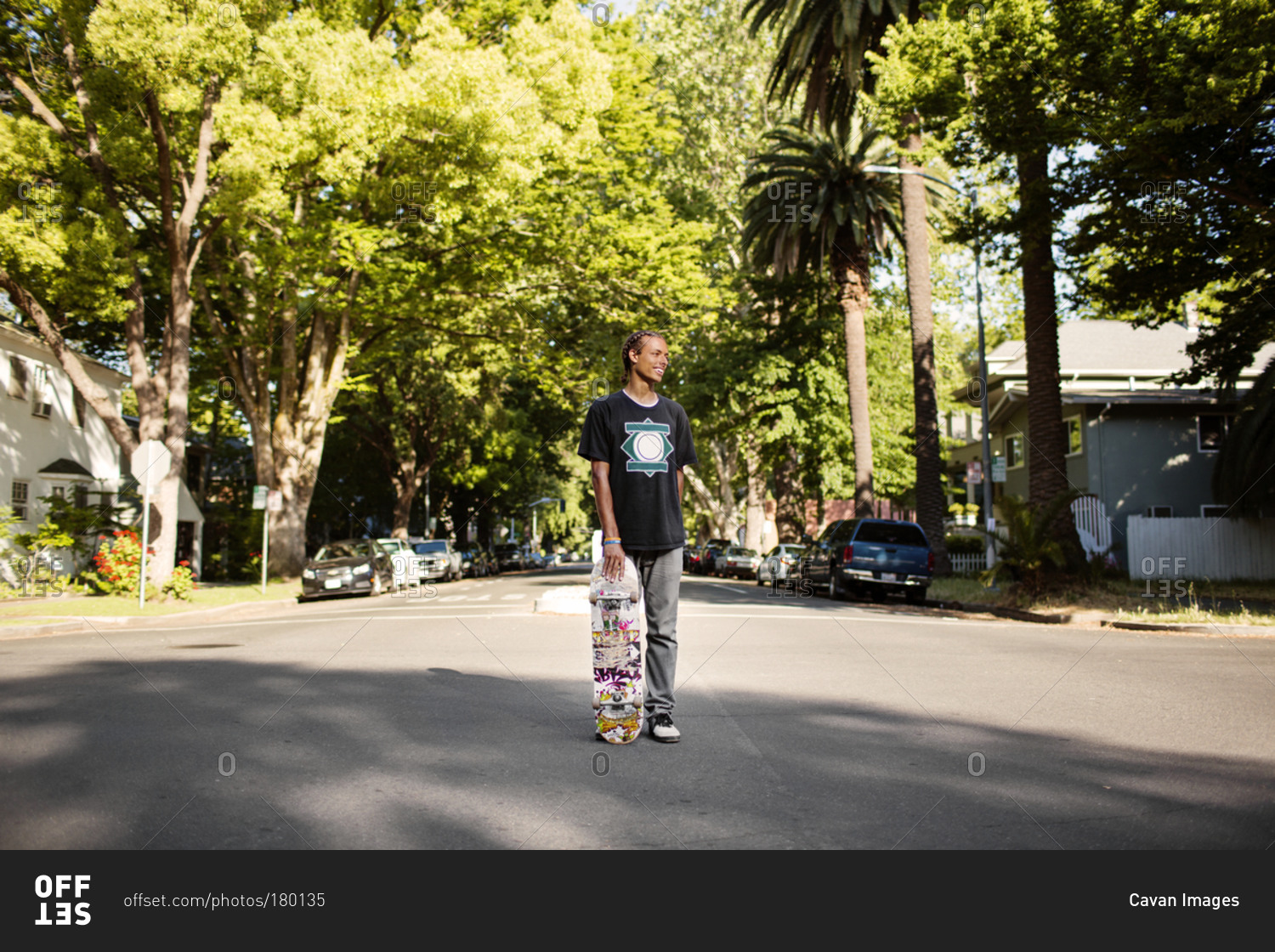 A young man stands in the street holding a skateboard