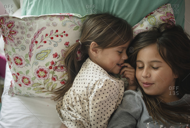 A girl and her sister cuddle in bed