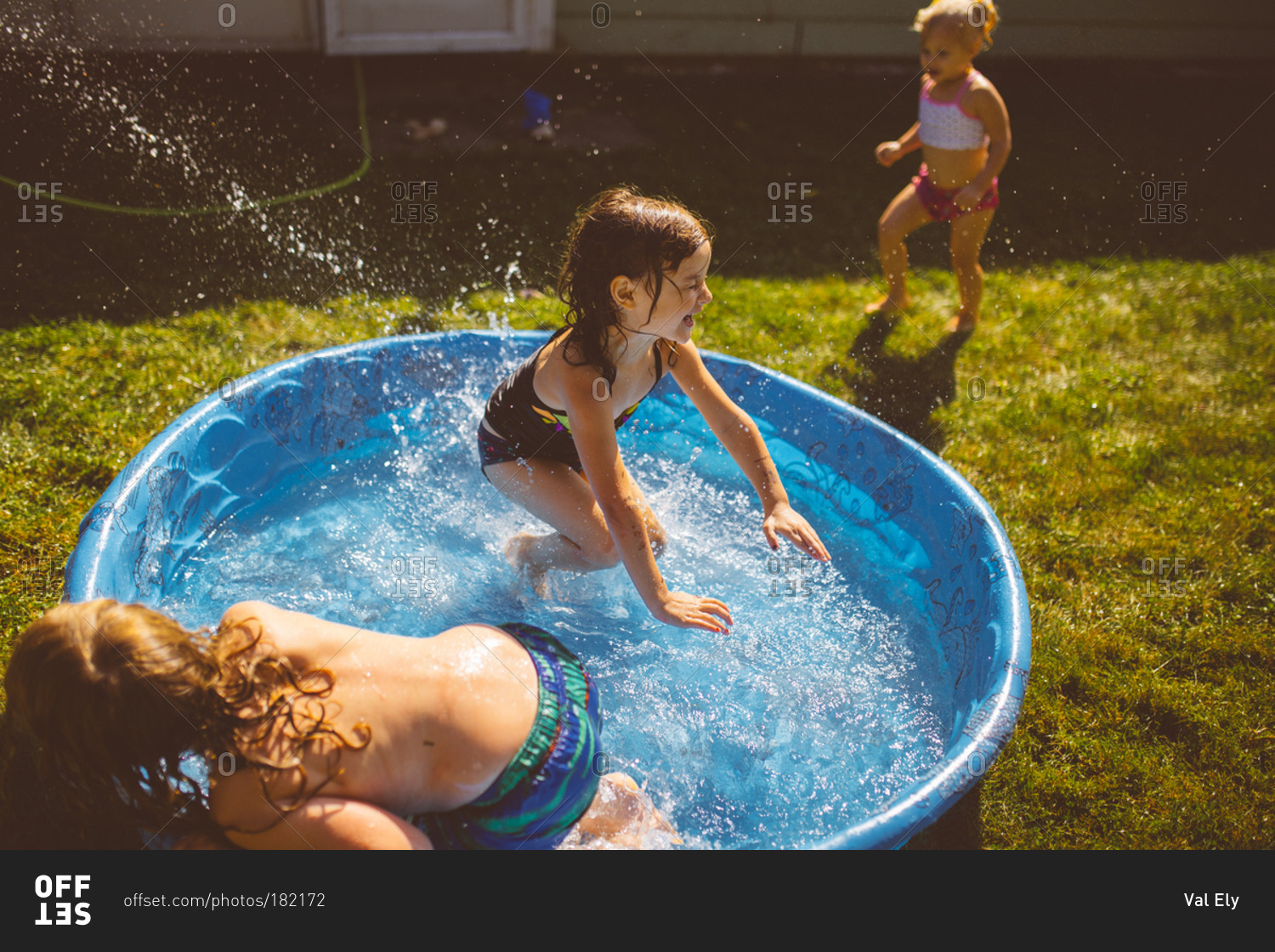 Three young children splash in backyard pool