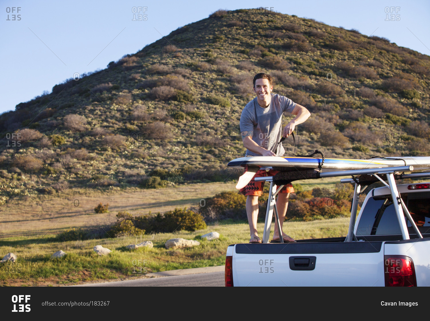 Man standing on back of truck with surfboard