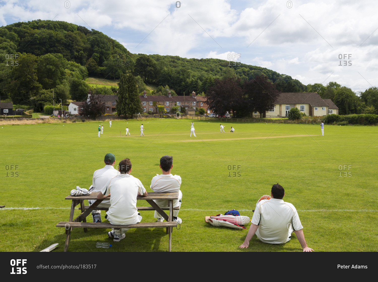 Players watching cricket match from picnic table