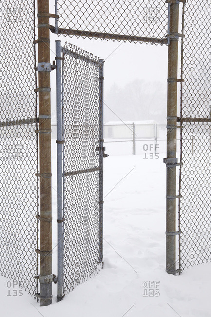 Chain link fence and gate to tennis court during snowstorm