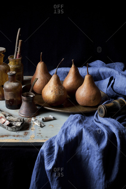 Still life of four pears on blue cloth with paints and bottles