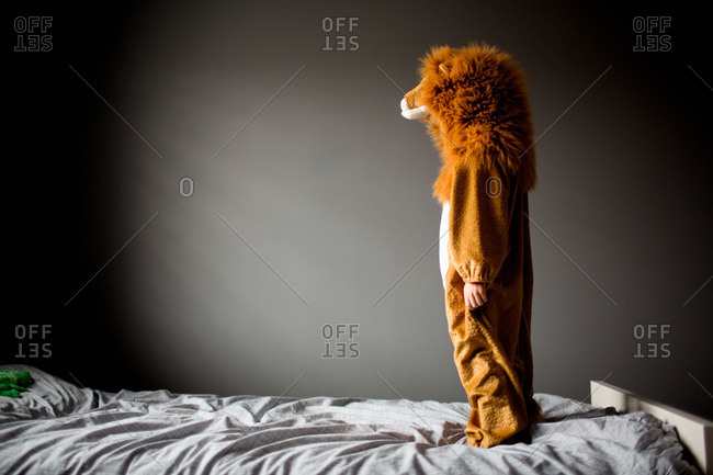 A boy stands on his bed in a lion costume