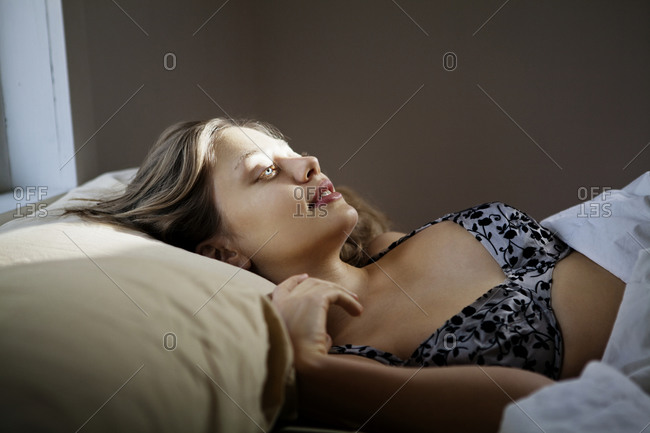 Woman laying awake in bed in bra stock photo - OFFSET