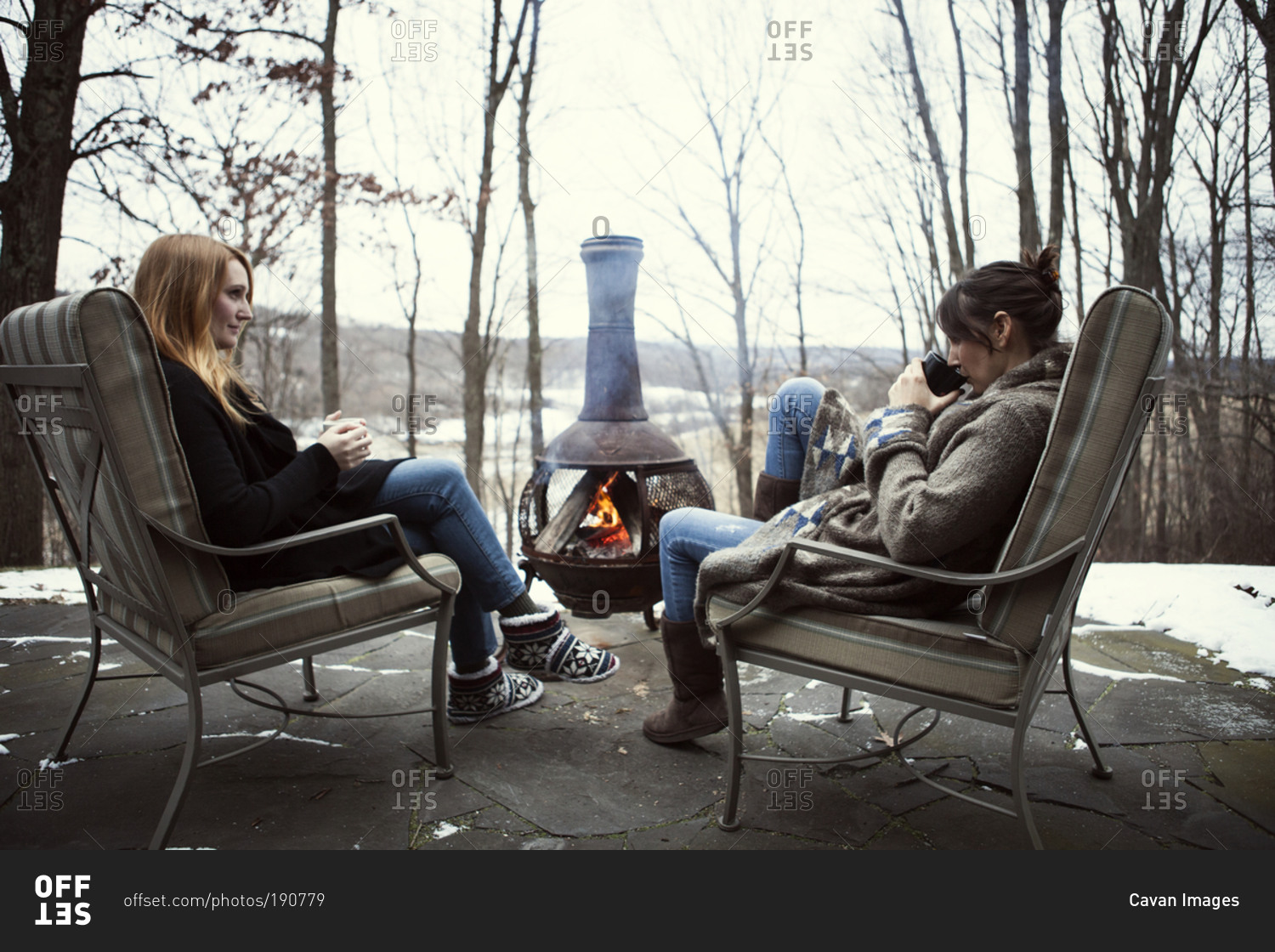 Two women drinking coffee by outdoor fireplace