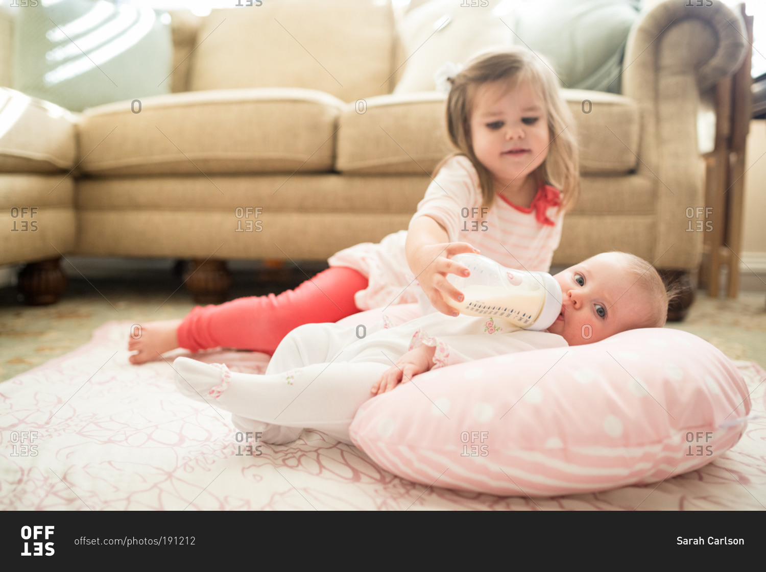 A little girl holds a bottle for her baby sister stock photo - OFFSET