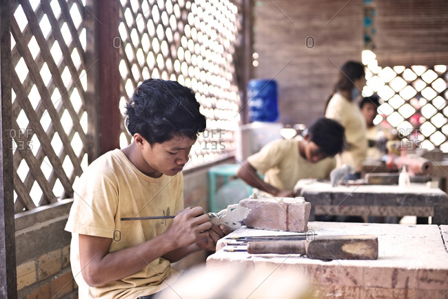 Siem Reap, Cambodia - December 20, 2014: Young man making a stone figurine