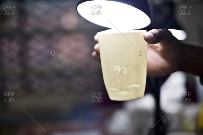 Person holding a ceramic cup under a lamp