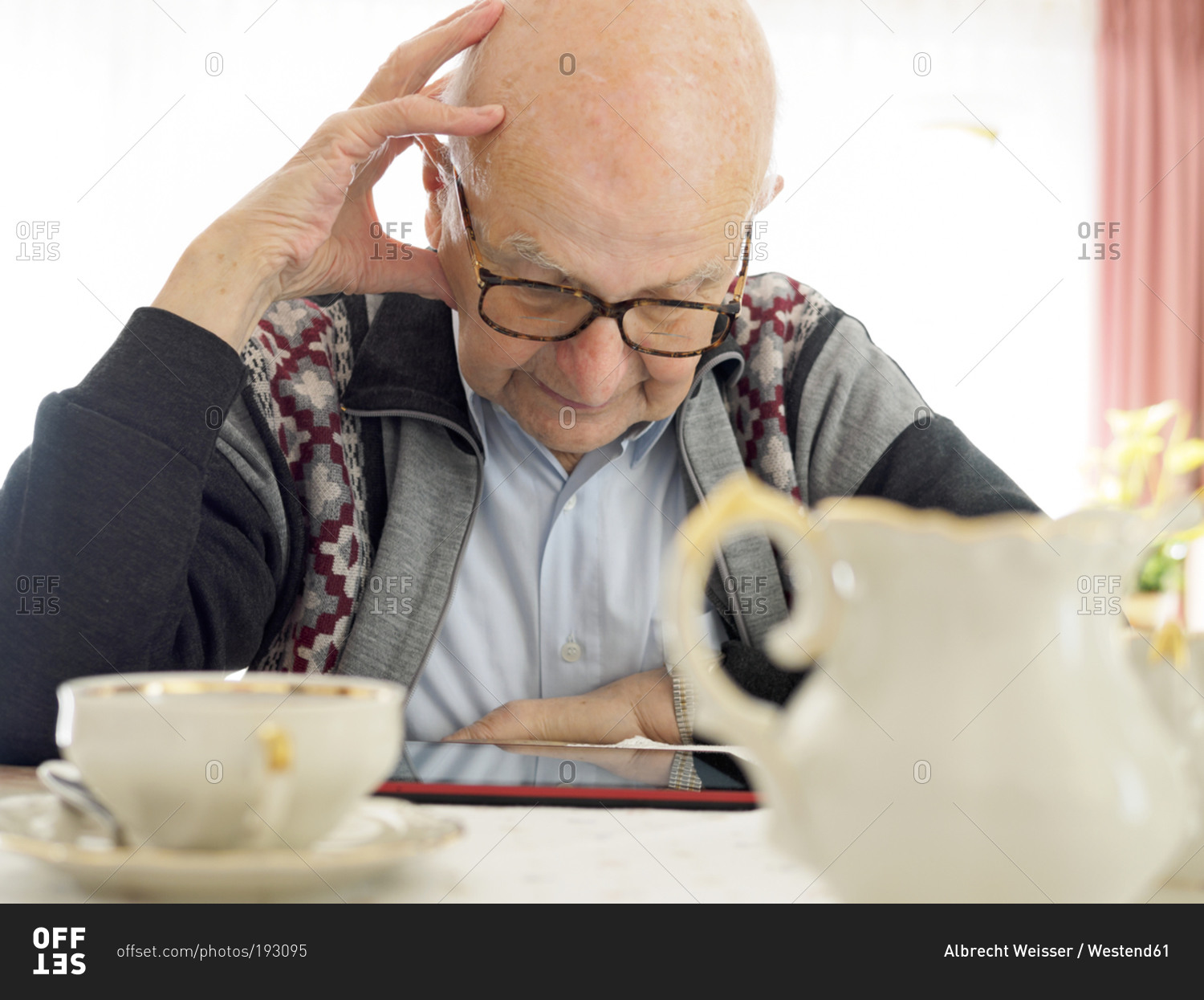 Old man sitting at table using digital tablet