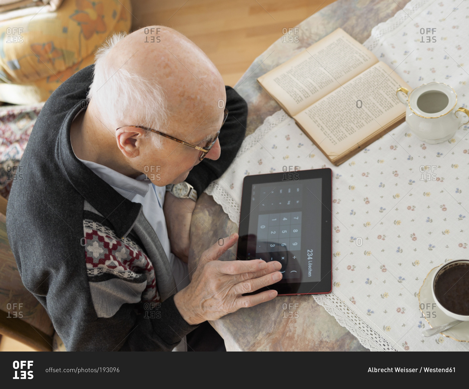 Old man sitting at table using digital tablet