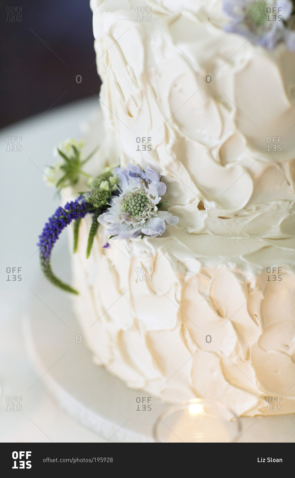 A small pale purple flower decorates a frosting covered cake