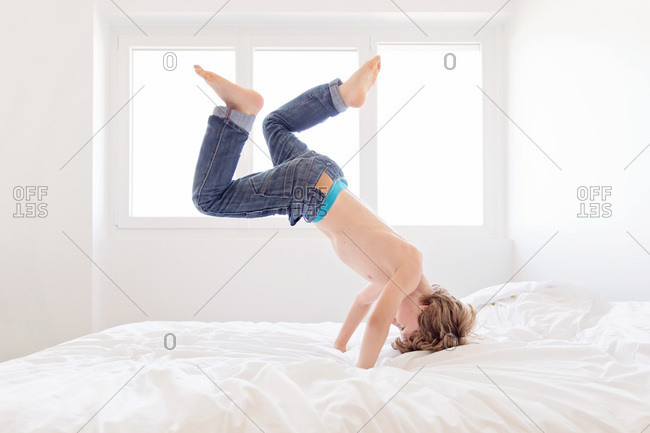 A boy does a headstand on a bed stock photo OFFSET