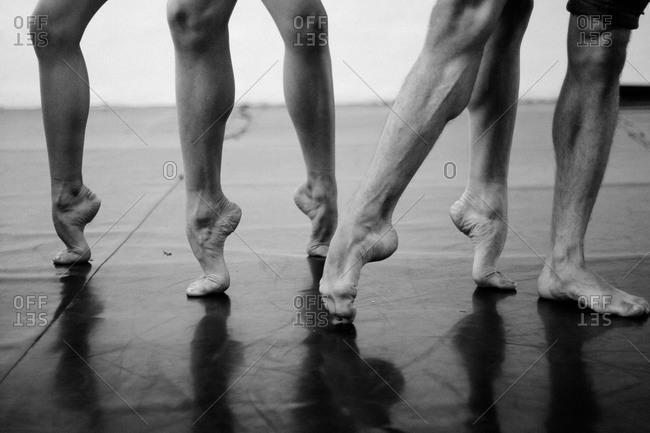 Muscular legs of three male dancers stretching their feet