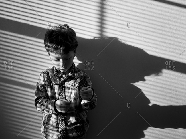 Young boy standing against a wall with shadows falling across