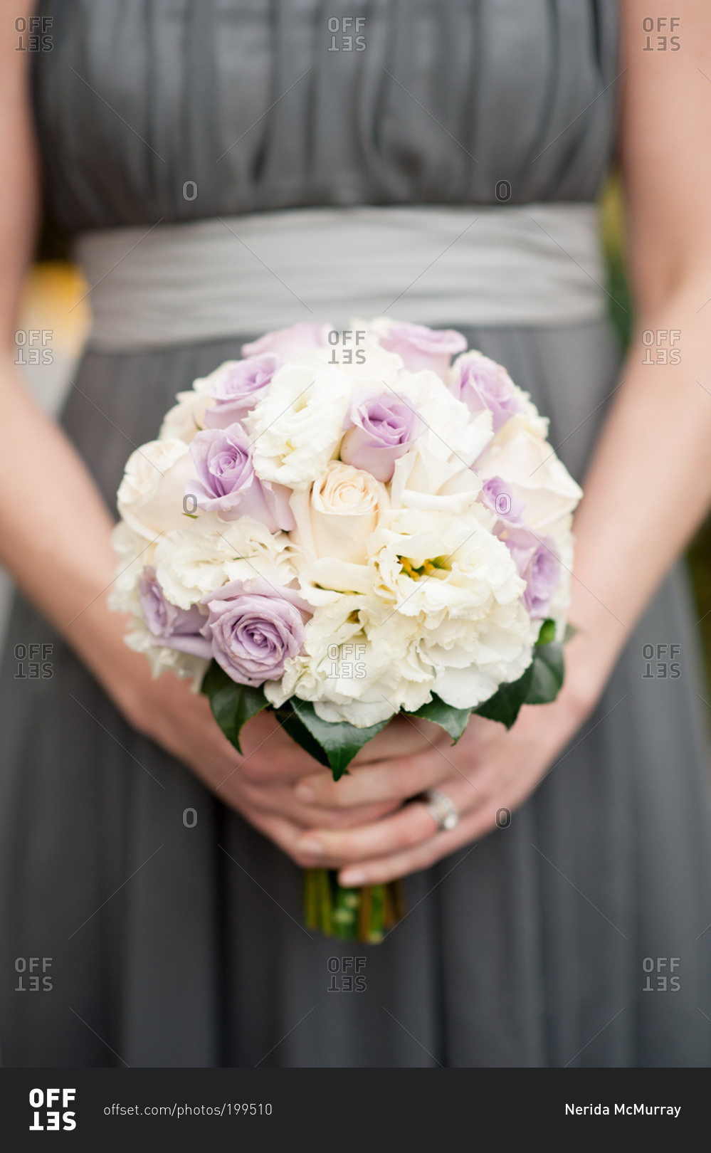 Bridesmaid in gray dress holding bouquet of pale purple and white flowers