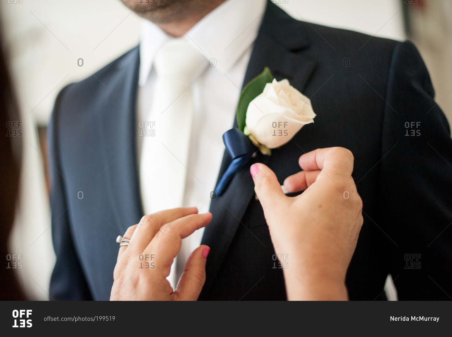 Woman pinning white rose boutonniere being pinned on the lapel of groom