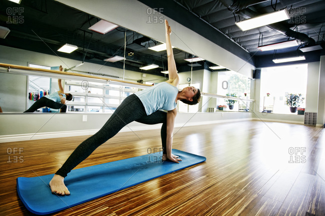 Young woman doing yoga on yoga mat in atmospheric yoga studio stock photo -  OFFSET